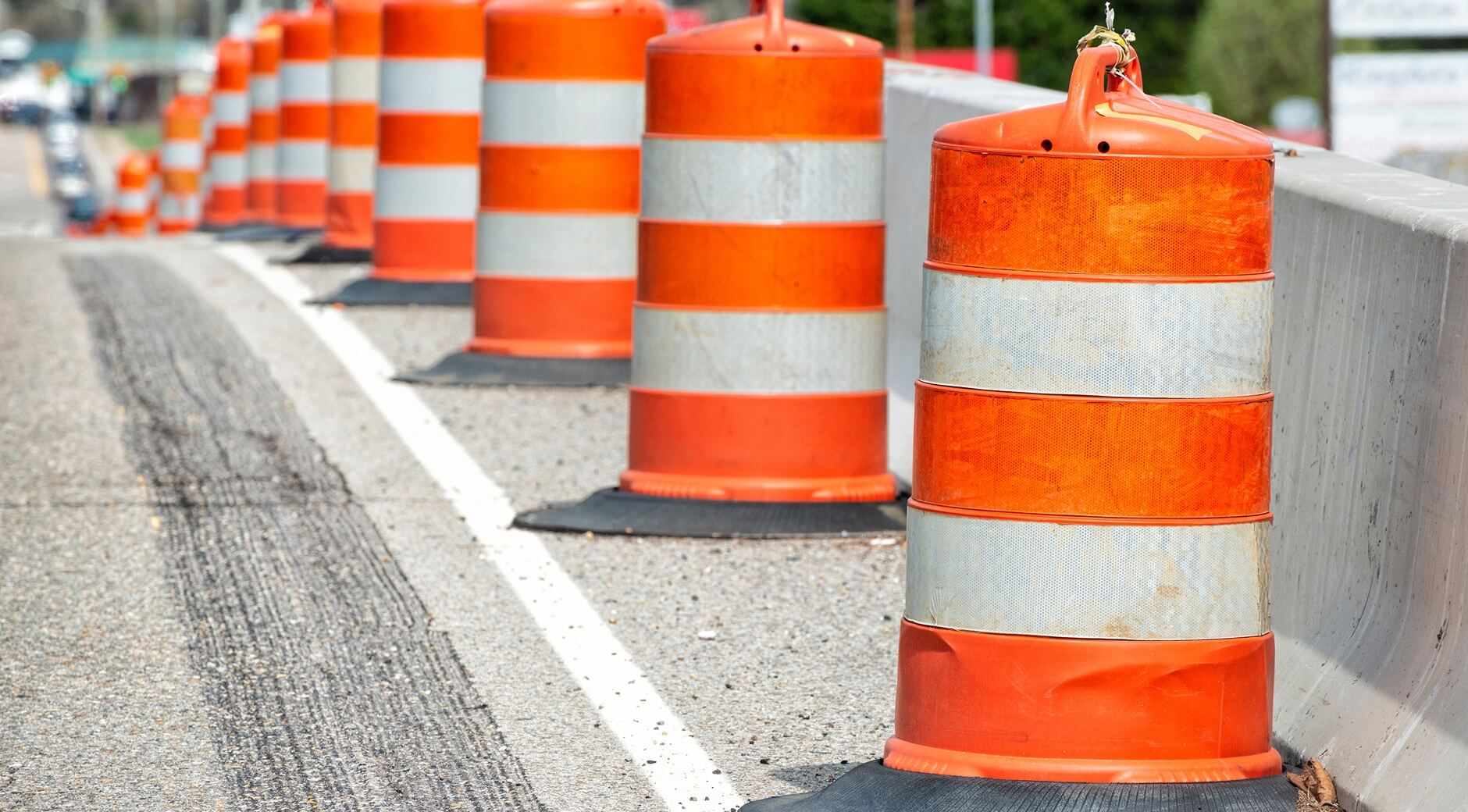 A line of orange and white traffic barrels set up along the side of a highway.